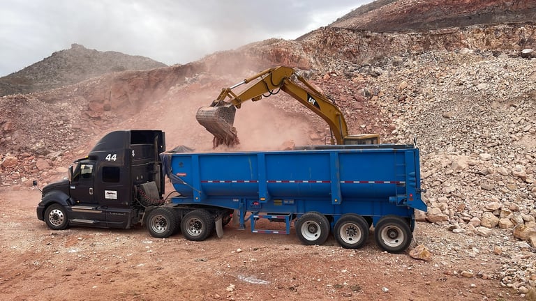 Excavadora amarilla cargando material en camión de volteo azul en sitio minero
