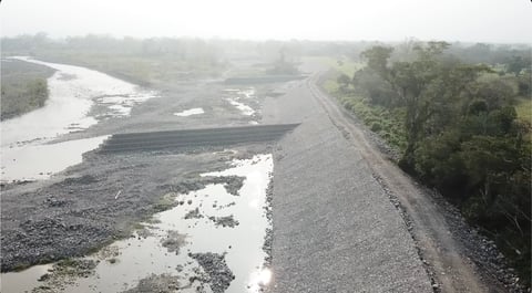 Aerial view of a winding river with gravel banks alongside a rural road lined with trees on a misty day