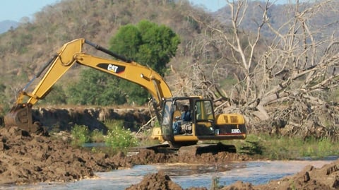 Excavadora CAT en terreno lodoso con árboles y colinas